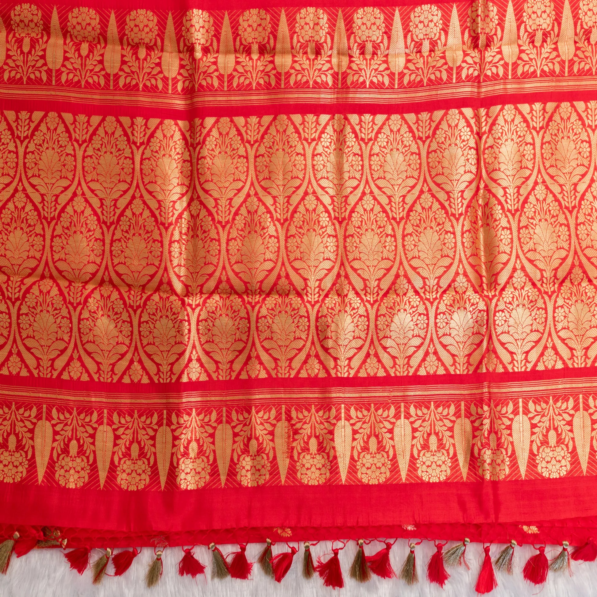 Red fabric with gold intricate patterns and tassels on a white background