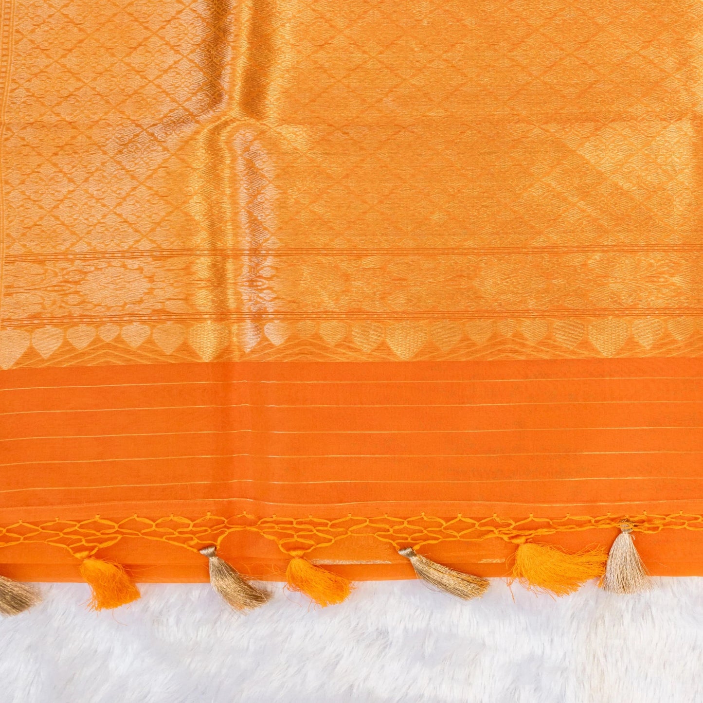Close-up of an orange fabric with intricate patterns and tassels on a white background
